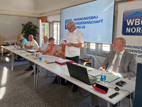 Eine Gruppe von Personen sitzt an einem Tisch und nimmt an einer Präsentation zu Wohnungsbau und Genossenschaft teil.