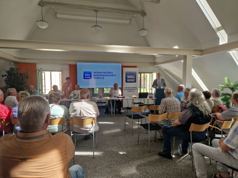 Eine Gruppe von Menschen sitzt in einem Saal und verfolgt eine Präsentation auf einer Leinwand.